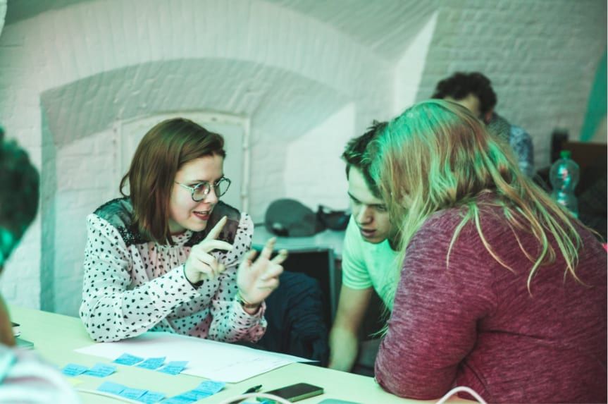 Iemand wijst naar een oranje postIt aan een muur